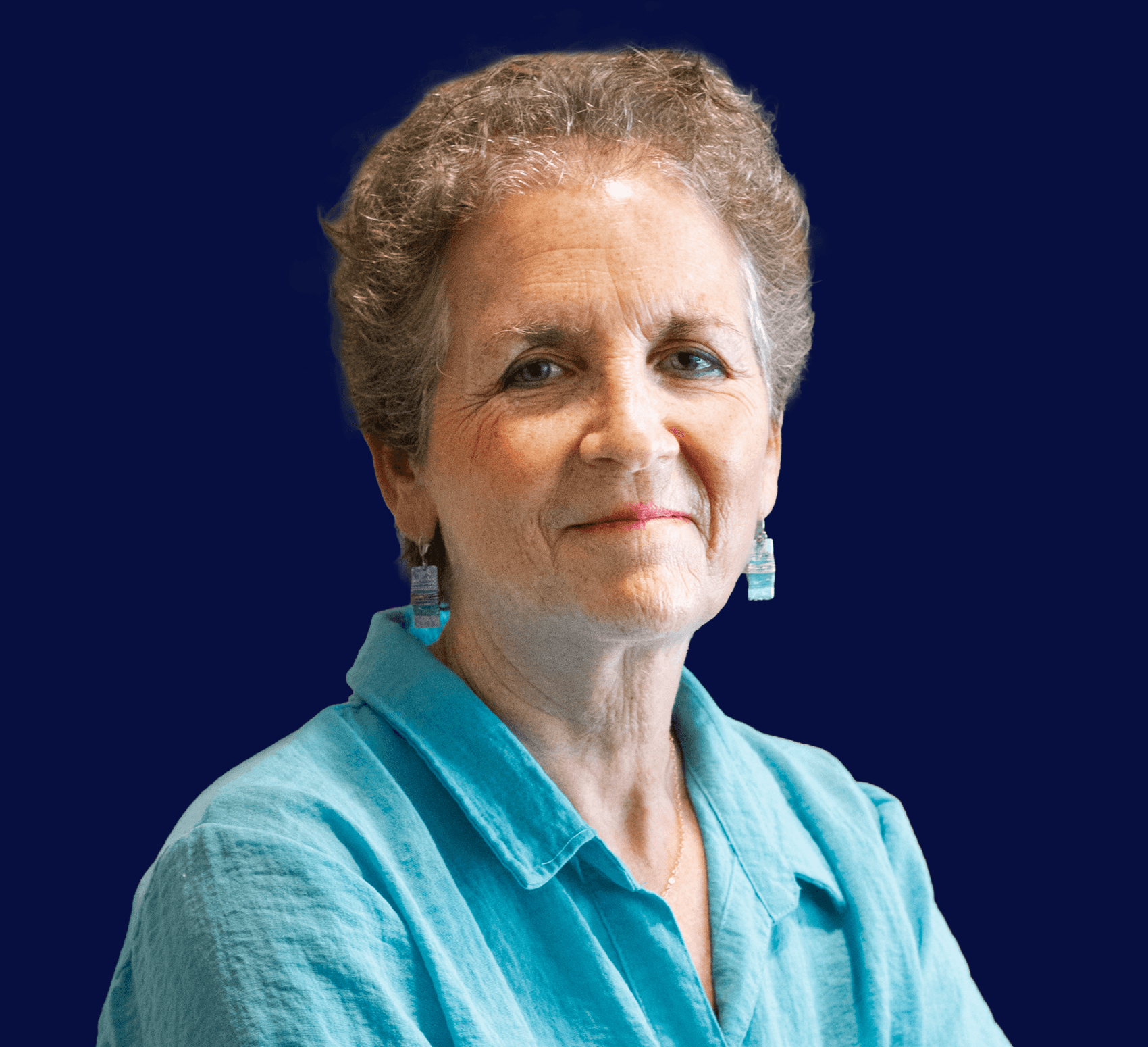 Headshot of woman with short, curly, light brown hair and fair skin. She wears a light blue collared shirt, against a navy background.