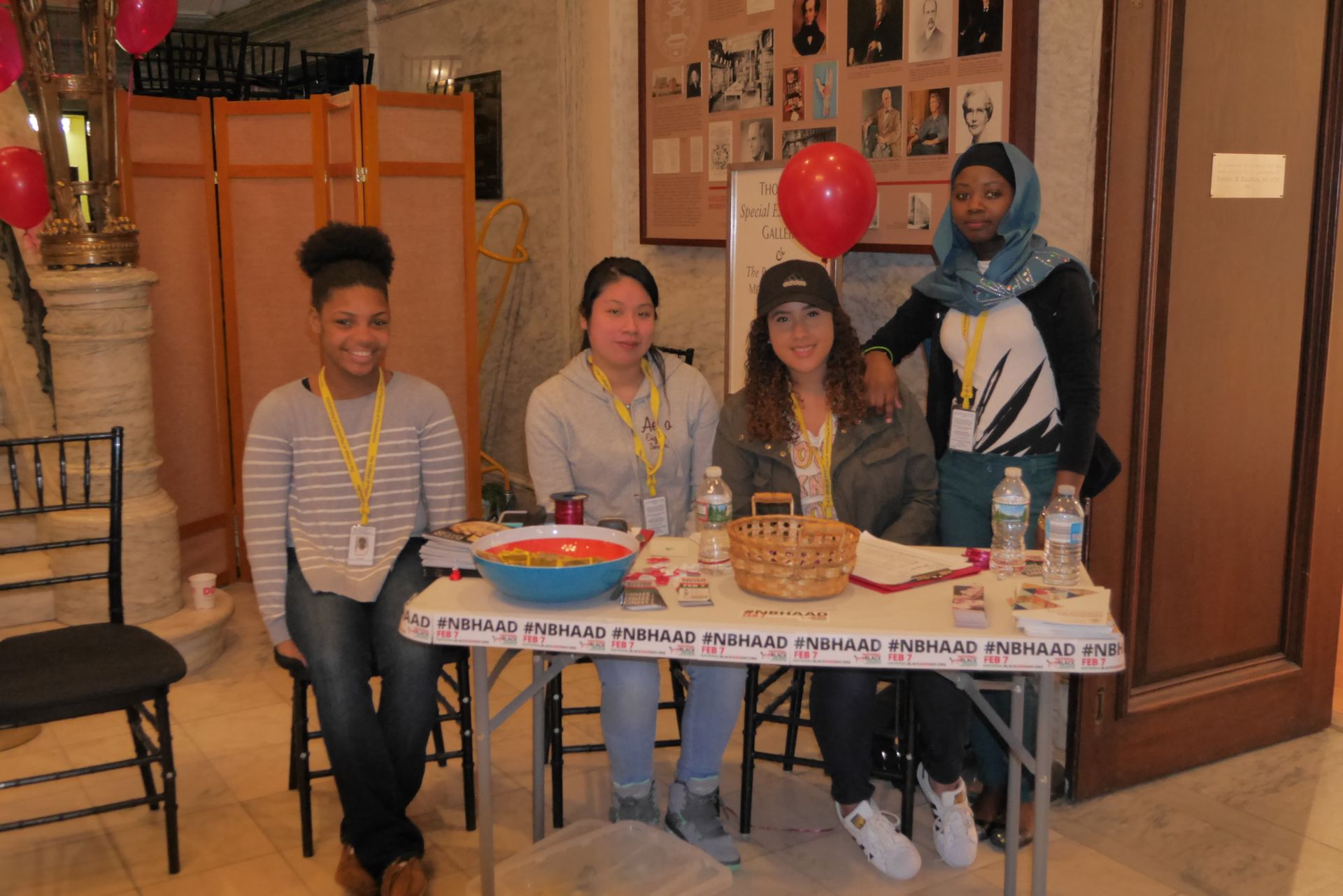 Four students in the Teva Pharmaceuticals Internship Program stand behind a registration table at National Black HIV/AIDS Awareness Day