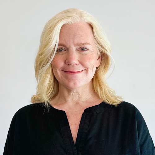 Headshot of a woman with light blonde, shoulder-length hair and a black top against a white background