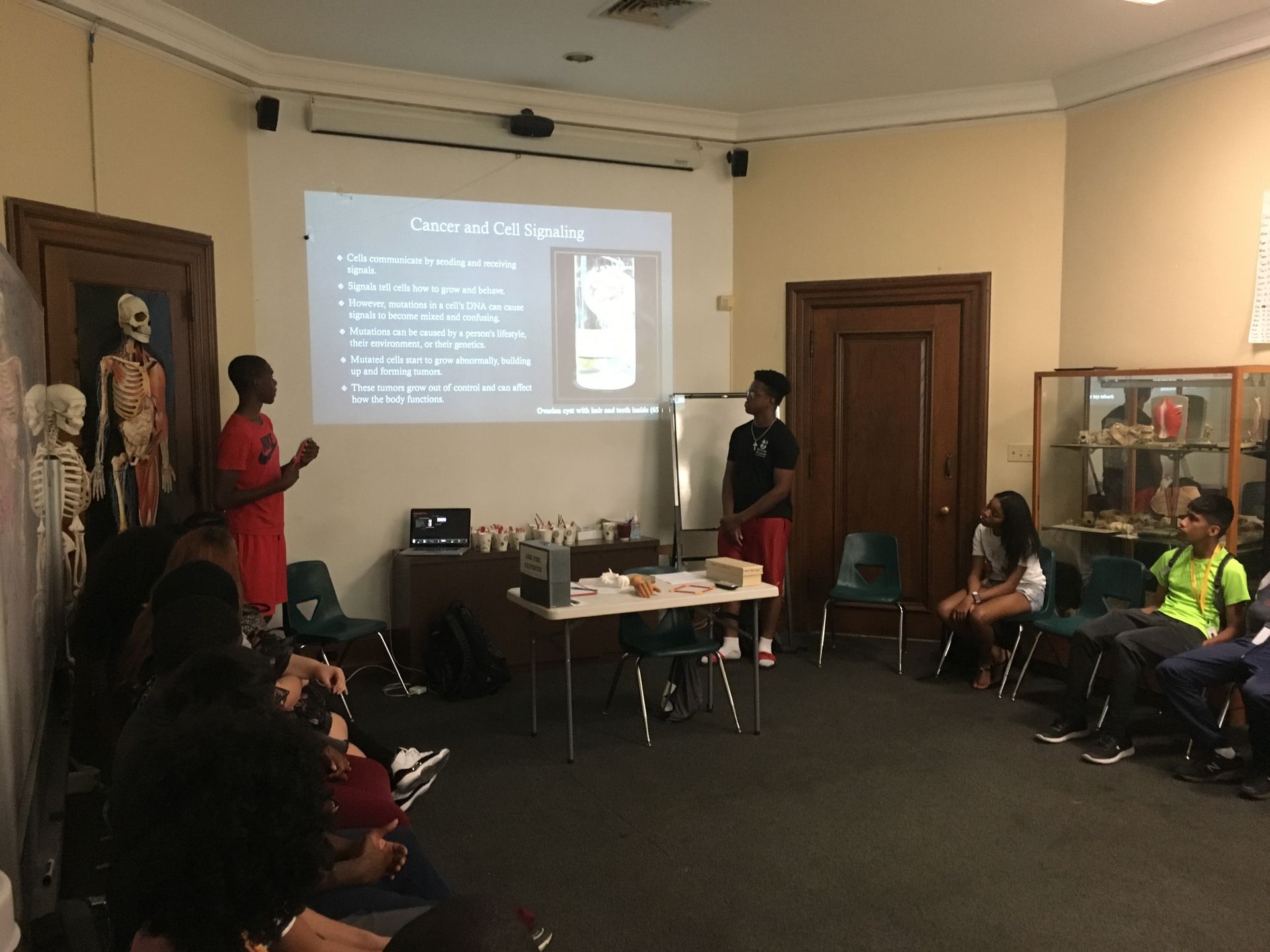 Lamina and Chaka, students in the Karabots Junior Fellows Program, deliver a lesson on cancer to students in the latest cohort in the program