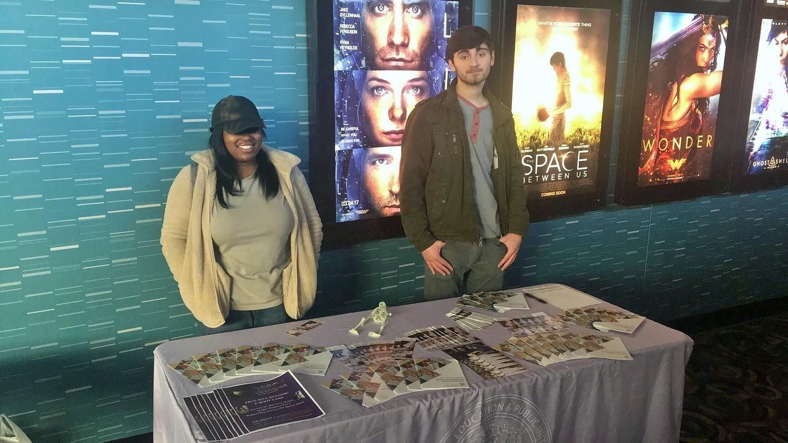 Students from the Teva and Out4STEM Programs stand at a table covered in literature about CEPI programming at Rave Cinemas at University City