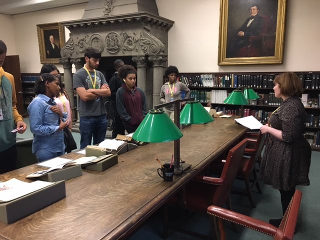 Students from the Teva Pharmaceuticals Internship Program stand in front of books on display for the Historical medical Library's exhibit for Banned Books Week. They are speaking with Library Assistant Caitlin Angelone.