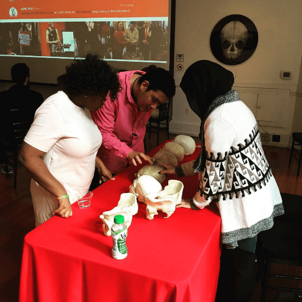 Sara, a student in the Karabots Junior Fellows Program, teaches two students about skull pathology by displaying a group of human skull replicas at World AIDS Day 2016